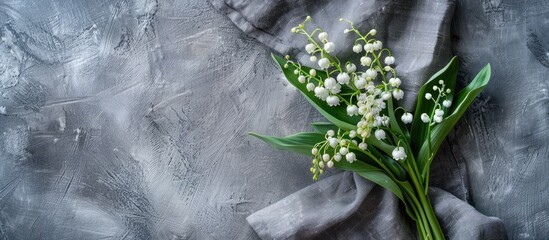 Wall Mural - Top view of a rustic greeting card concept with a bouquet of white lilies of the valley and green leaves on a gray linen background offering ample copy space for cover design