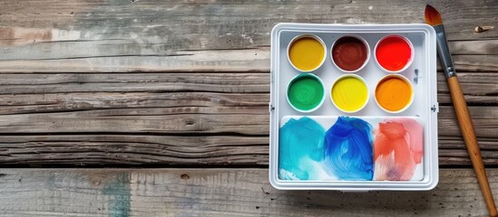 Aufkleber - Watercolor paint and brush are displayed neatly in a white plastic box on a vintage wooden surface seen from above with copy space image