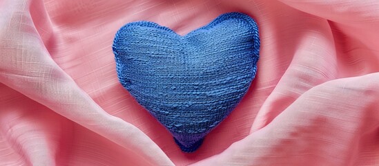 Poster - Heart shaped blue textile with embroidered lines set against a pink fabric backdrop ideal for a copy space image