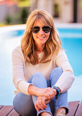 Poster - Attractive mid aged woman sitting in the garden with the pool in the background