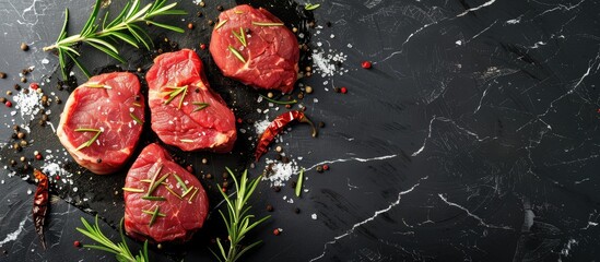 Poster - Copy space image of raw beef steaks with rosemary dried cayenne peppers and scattered salt on a black marble surface