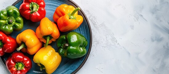 Poster - A variety of fresh bell peppers in different colors arranged on a blue plate against a white backdrop The image focuses on the multicolored peppers from a top view leaving space for text or other ele