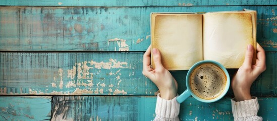 Poster - Woman s hands holding a blank book and a cup of coffee on a bright background with copy space image