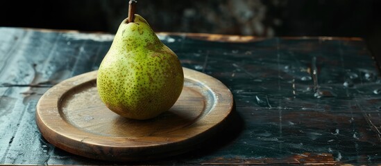 Poster - A raw green pear on a wooden plate against a black backdrop provides ample copy space image