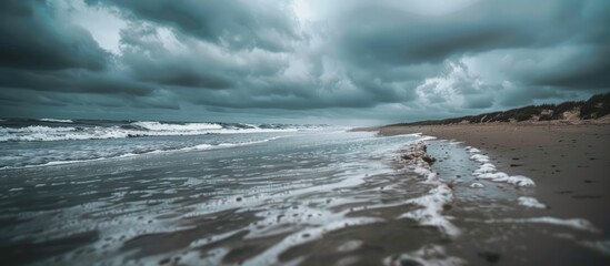 Poster - The sandy shore is lined with waves under a cloudy sky with an available copy space image of the sea