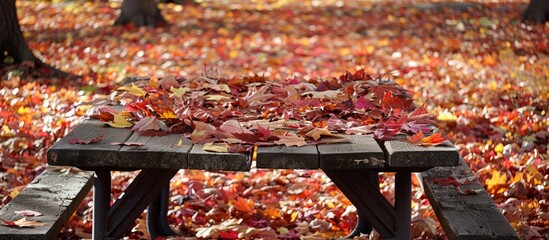 Poster - In a park fallen red and gold autumn maple leaves surround a picnic table creating a picturesque scene with copy space image available