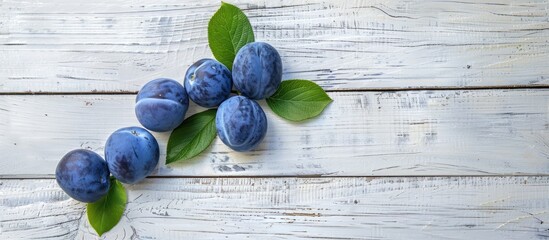 Poster - Three blue plums and a green leaf on a white wooden surface with ample copy space image