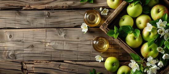 Leinwandbilder - Top view of a wooden table with a wooden box filled with ripe green apples a branch of white flowers and a glass and bottle of cider with copy space image