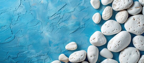 Poster - A messy arrangement of white textured pebbles on a blue table with copy space image