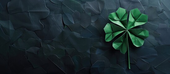 Emerald green origami clover leaf on black paper background with Happy St Patrick s Day lettering for a festive postcard with copy space image