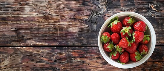 Poster - A top view copy space image features fresh strawberries in a white bowl on a rustic wooden table