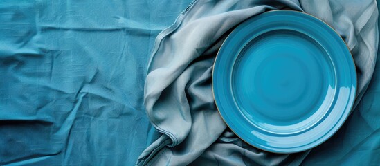 Poster - Bird s eye view of a blue plate on a tablecloth with a napkin offering a blank canvas for your design in the copy space image