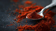 © VK Studio - A spoonful of rich red spice lies on a textured dark surface, surrounded by scattered spice granules, evoking warmth and flavor.