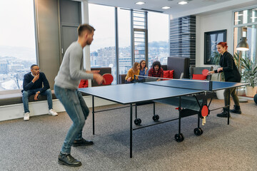 Wall Mural -  Business colleagues take a break from work to enjoy a game of table tennis, fostering teamwork and camaraderie in the workplace