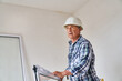 © Robert Kneschke - Side view of senior male carpenter standing with window frame at incomplete house site