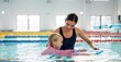 © peopleimages.com - Instructor, teaching and child in pool, swimming or woman with smile, proud or helping girl in water. Bathing suit, happy or learning with teacher in school for training of kid, sports or competition