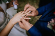 © Raivo - Cesis, Latvia - July 12, 2024 - Close-up of a groom placing a wedding ring on the bride's finger during their ceremony. The bride holds a bouquet in her other hand.