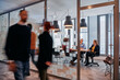 © .shock - In the dynamic hustle and bustle of a business environment, a group of young business professionals walk down the corridor next to their office, while their colleagues collaborate inside, symbolizing