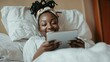 © mutter - Millennial african girl reading blog on digital tablet while lying in bed with free space around her
