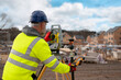 © Iryna - Construction Worker Using Surveying Equipment on a Residential Building Site During Daylight Hours