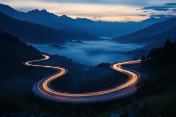 Wall Mural - A long exposure photo of the lights from cars on a winding mountain road at dawn, with mist in the valley below and mountains in the background.