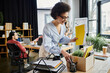 © LIGHTFIELD STUDIOS - Happy african american woman packing her items during lay off, colleagues on backdrop.