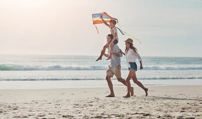 Wall Mural - Family, flying kite and running on beach together for holiday, travel or vacation in summer. Carry, energy or love with mother, father and son on sand at coast by ocean or sea for bonding or freedom