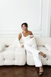 © Alex Barera - Sophisticated brunette woman in a crisp white pantsuit sits elegantly in a white interior studio. Refined and modern corporate style