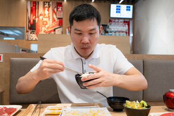 Man using chopsticks eating rice in black bowl in Japanese Shabu restaurant