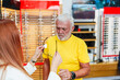 © Dusko - Good looking gray hair man choosing eyeglasses frame in a modern optical store. Female seller specialist helps him to make right decision.