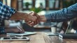 © Johannes - Two entrepreneurs shaking hands in a co-working space, finalizing a business deal with laptops and smartphones on the table, successful technology partnership