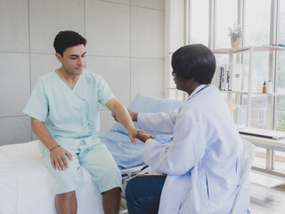 Wall Mural - Portrait patient caucasian man with woman nurse carer physical therapist African-American two people sitting talk helping support give advice and holding hand arm inside hospital indoor room service.