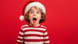 © Nicolai - adorable surprised kid wearing a Santa Claus hat and striped sweater on a red background