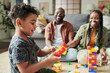 © pressmaster - Side view of adorable little boy in casual attire sitting on the floor in front of his parents and playing constructor at leisure