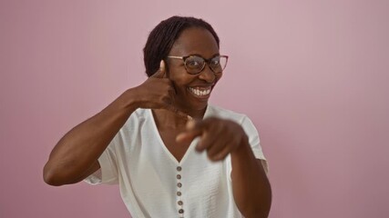 Wall Mural - Young african american woman with glasses standing and wearing a t-shirt, making a phone gesture with hand and smiling over isolated pink background - concept of communication and positivity