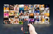 © Prostock-studio - A hand holds a black TV remote in front of a large screen displaying a grid of various images. The screen is displaying a variety of scenes, including people eating, working, and relaxing.