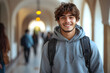 © Gonzalo - Smiling young male student with backpack, standing in a bright hallway with arched ceilings