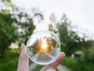 Wall Mural - a person is holding a clear glass ball that is reflecting the sunrise over a small country road, sel