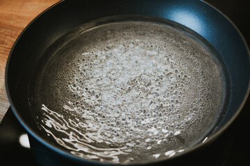 pot with boiling water with bubbles close-up on black kitchen stove for cooking pasta