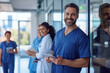 © GraysonStock - Portrait of smiling young male nurse in blue scrubs standing against wall at hospital
