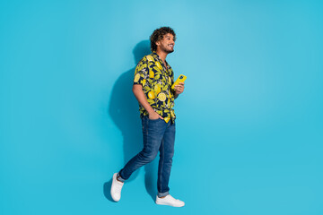 Full size photo of cool man dressed print shirt jeans holding smartphone look at sale empty space isolated on blue color background