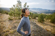 © Jovo Jovanovic/Stocksy - Tired happy athlete with earphones looking at landscape after run