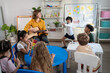 © Kawee Srital-on/Stocksy - Caucasian young woman teacher playing guitar with student in school.