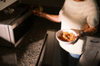 © Serena Burroughs/Stocksy - woman in kitchen using microwave to heat up leftovers