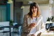 © BONNINSTUDIO/Stocksy - Businesswoman smiling using smartphone in modern office space