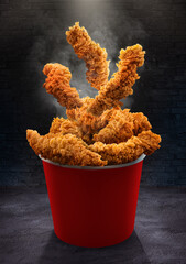 Fried chicken Hot crispy strips crunchy pieces of chicken breast tenders in a Bucket - a large Red box on the black table in the restaurant	
