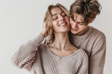 Wall Mural - A young Russian man wearing jeans and a sweater put a silver necklace around the neck of his beautiful blond wife against a white background