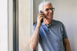 © VICTOR TORRES/Stocksy - Happy senior man in glasses talking on cellphone near window