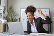 © amnaj - Young office worker is raising her fist in the air, excited about a win she just had while working on her laptop