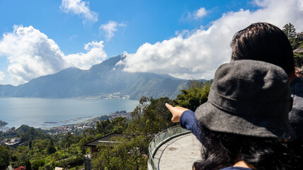 Wall Mural - Back view of a tourist couple looking at Batur Lake and Trunyan Hill in Bali. The couple enjoys the scenic view, highlighting the natural beauty of the landscape. Travel and nature photograpy concept